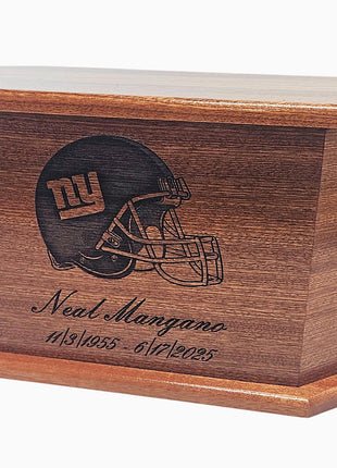 A wooden box with a football helmet embossed on it, and the text "Neal Mangano" and "19/5/55 - 6/2025" printed on it.