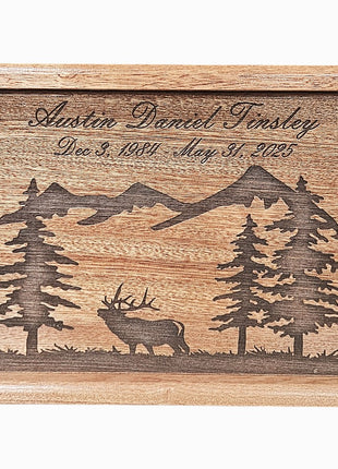 A wooden urn or urn-like container with a carved design depicting a deer and mountains. The text on the container reads "Austin Daniel Tinsley Dec. 3, 1981 - May 31, 1985".