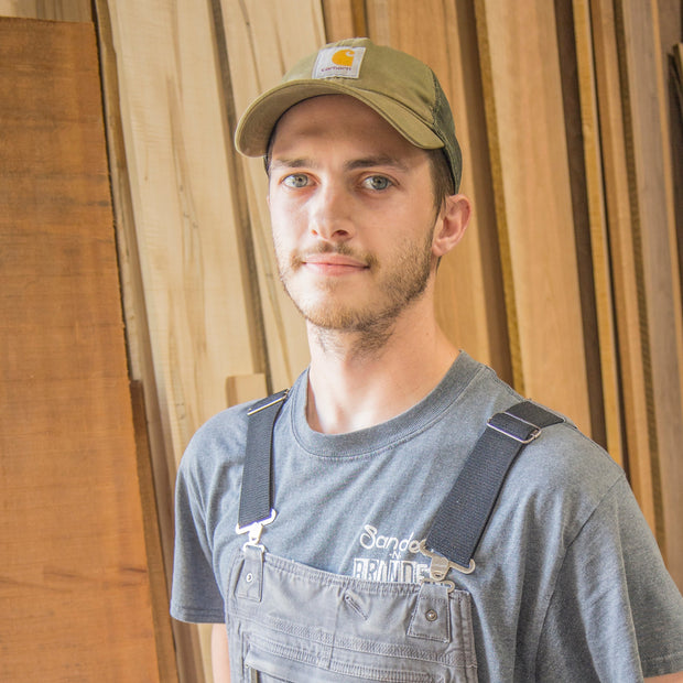 Man wearing a cap and overalls standing in front of wooden panels