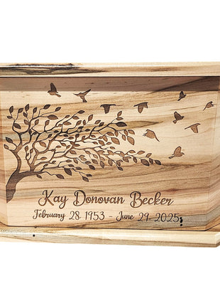 A wooden box with a tree design and birds on it, engraved with the name "Kay Donovan Becker" and the dates "February 28, 1953 - June 29, 2025".