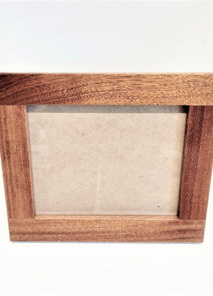 A wooden picture frame with a blank white paper inside, sitting on a white surface.