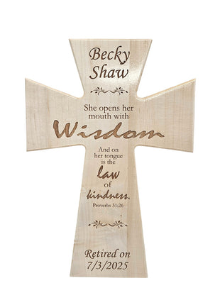 A wooden cross with the name "Becky Shaw" engraved on it, along with a Bible verse from Proverbs 31:26.