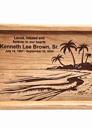The image is a wooden urn or urn-like container with a carved design depicting a beach scene with palm trees. The text on the urn reads "Loved, missed and forever in our hearts Kenneth Lee Brown, Sr. July 14, 1961 - September 23, 1974".